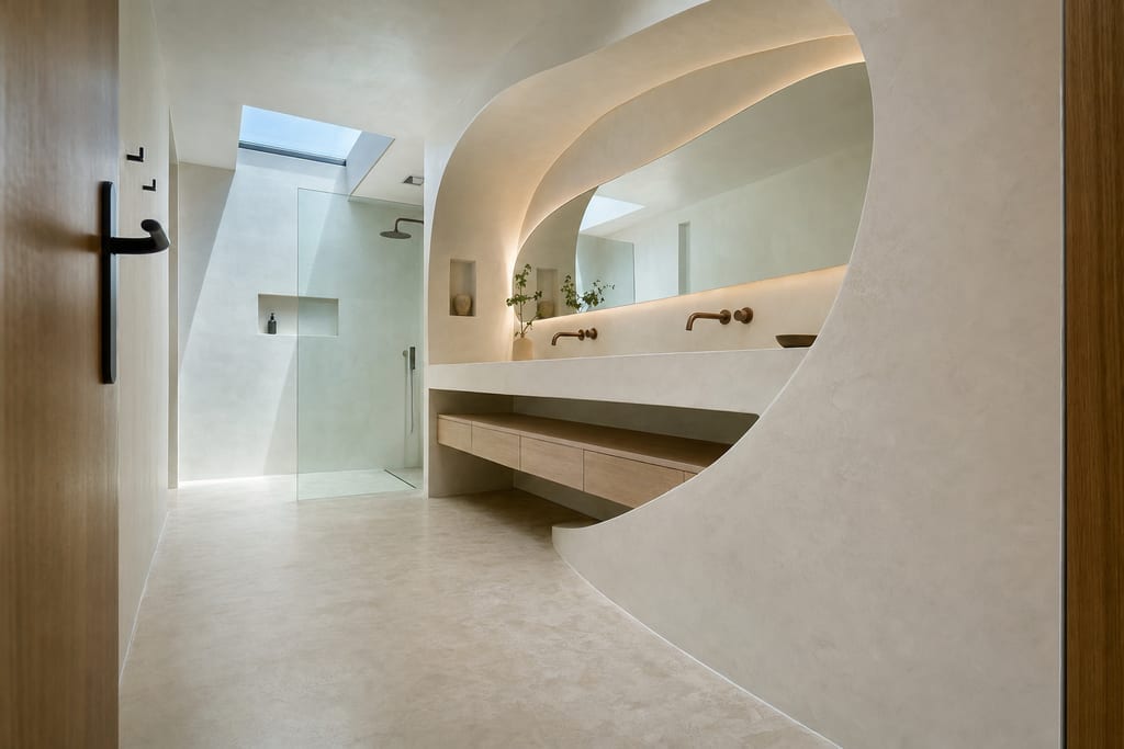 Low-angle view of sculptural curved plaster vanity and frameless shower in a stone mat bathroom
