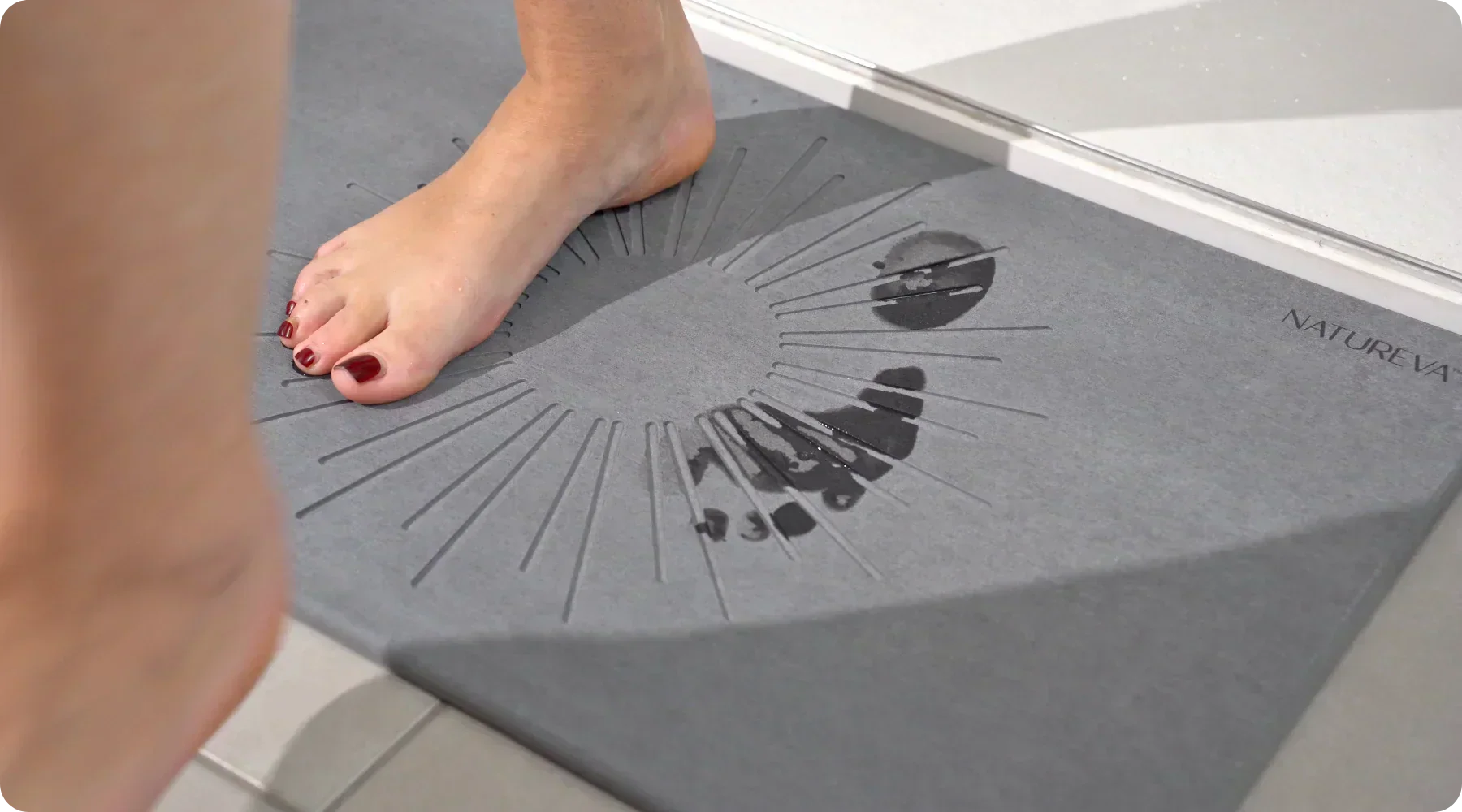 Feet on a stone bath mat in a bathroom demonstrating quick-drying surface